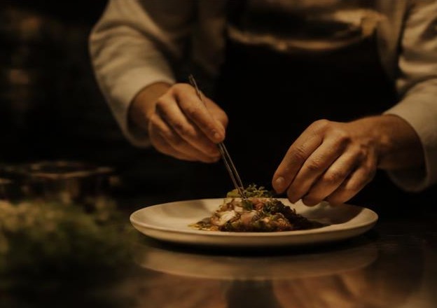 Film still of a chef plating a dish in warm light